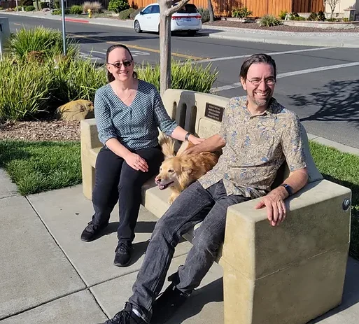 man and woman sitting on bench with dog