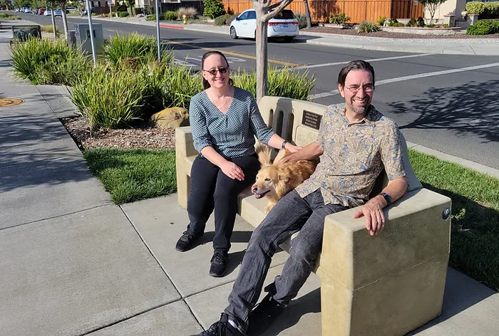 man and woman sitting on bench with dog