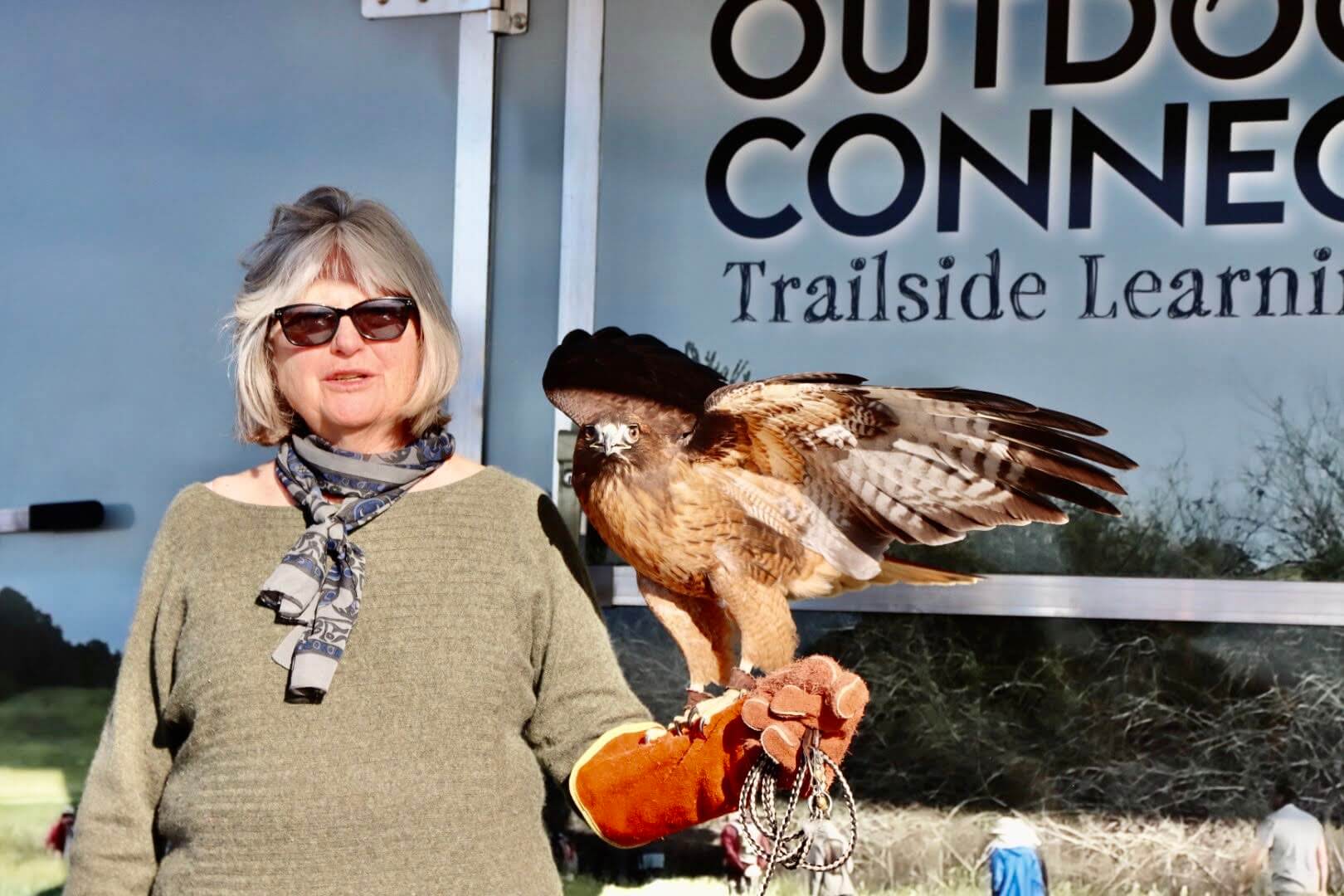 Wildlife Rescue volunteer with a red-tailed hawk in front of the Outdoor Connection mobile classroom